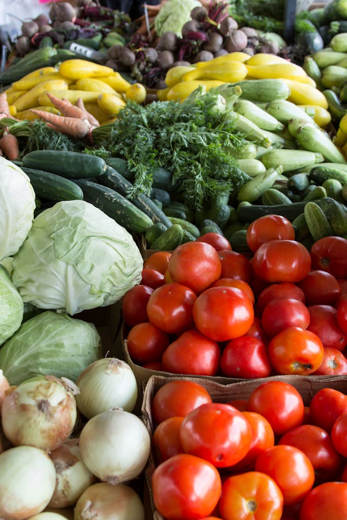 Présentation de légumes frais avec des tomates, du chou, des oignons des courgettes sur un étal de marché.
