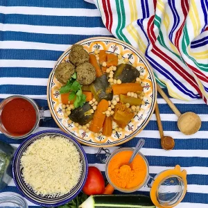 Un couscous aux legumes servi avec de la semoule dans un décor oriental. Un pot de safran en poudre est posé sur la table avec une cuillère dedans.